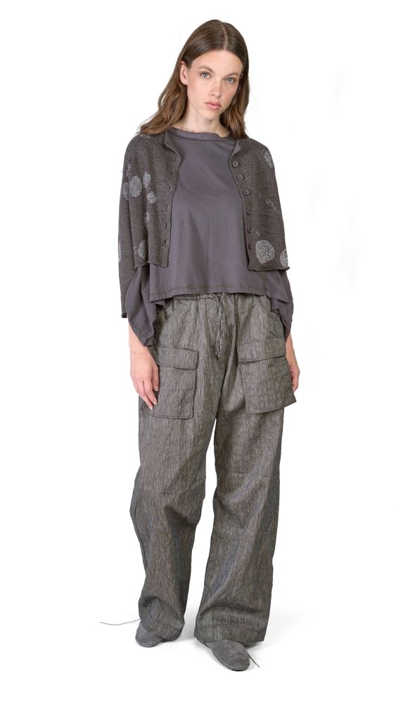 Frau trägt graues oversize Hemd mit Stickereien und weite, bequeme Stoffhose mit Taschen.