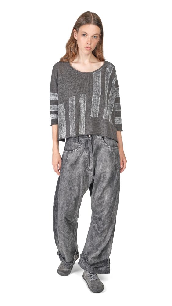 Frau trägt grauen oversized Pullover mit Streifen und weite, geflickte Jeanshose, bequeme Schuhe.