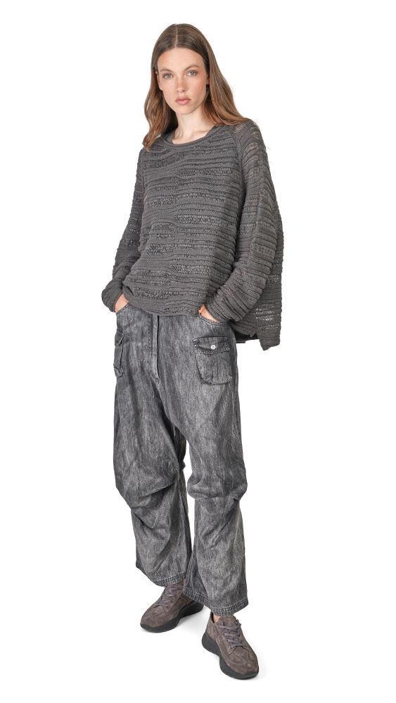 Frau trägt grauen oversized Strickpulli mit weitem, abgewetztem Hosenrock und Sneakern.