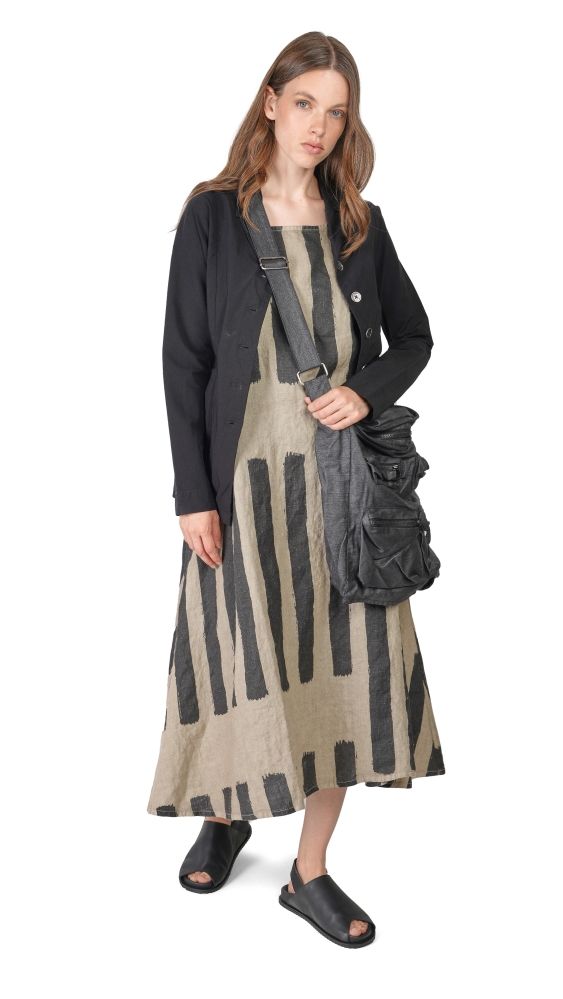 Frau trägt langes gestreiftes Kleid mit schwarzem Blazer und Sandalen, trägt Umhängetasche.