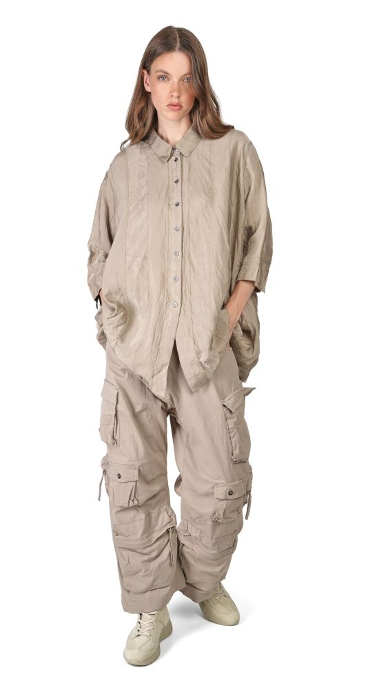 Frau trägt beigefarbenen oversized Overall mit vielen Taschen und Knöpfen, kombiniert mit Sneakern.