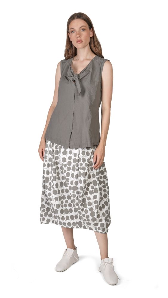 Frau trägt graues Sleeve-Top mit Knoten und weiß-grau gemusterten Rock, weiße Sneaker.