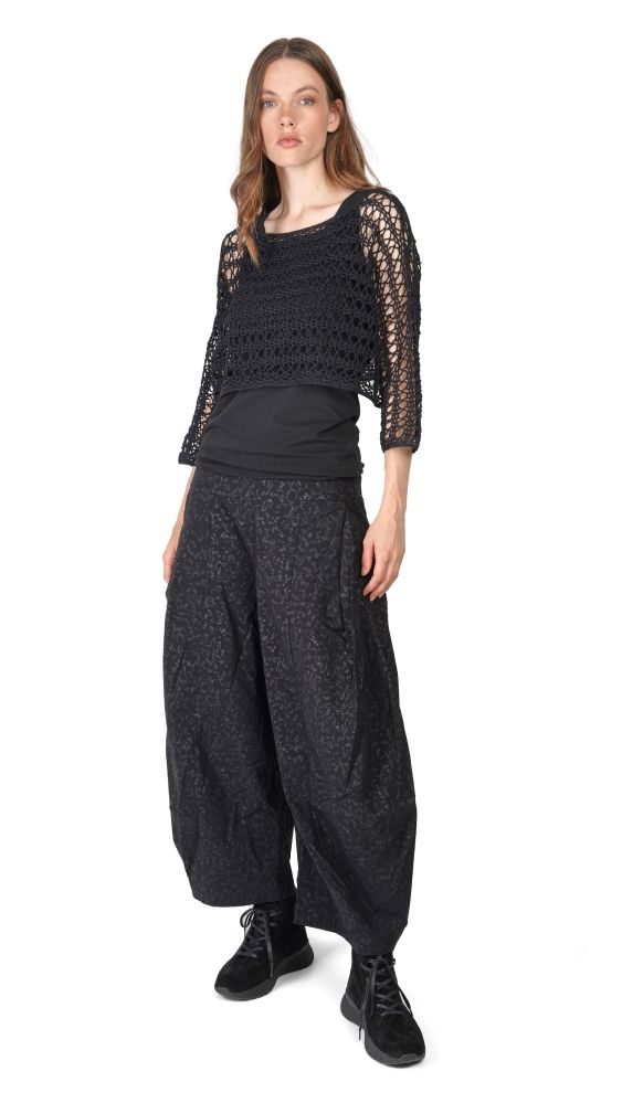 Frau trägt schwarzes oversize Top mit Spitzenmuster und weite, gemusterte Hosen, schwarze Sneaker.