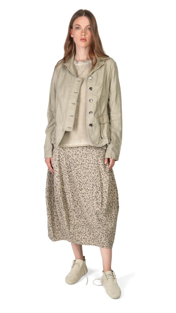 Frau trägt beigefarbenen oversize-Jakett, floralen Rock und helle Sneakers.