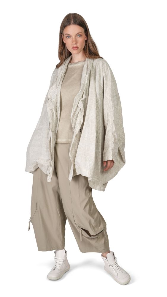 Frau trägt oversized beige Strickponcho mit weitem Schnitt, beige Hosen und weiße Sneaker.