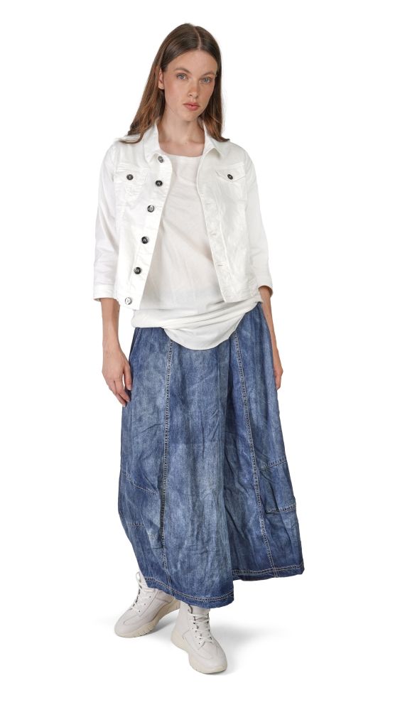 Frau trägt weiße Jacke, helles Shirt und weite blaue Jeans mit weißen Sneakern.