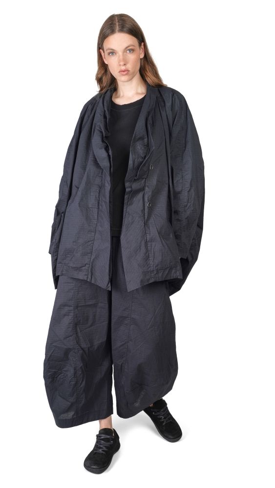 Frau trägt oversized schwarzen Mantel mit weitem Schnitt und schwarzen Pantalons, schlichtes schwarzes Top.
