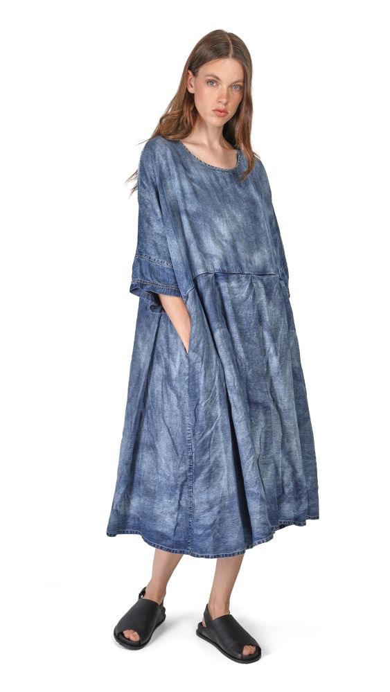 Frau trägt langes, blau gefärbtes Denim-Kleid mit weitem Schnitt und schwarzen Sandalen.