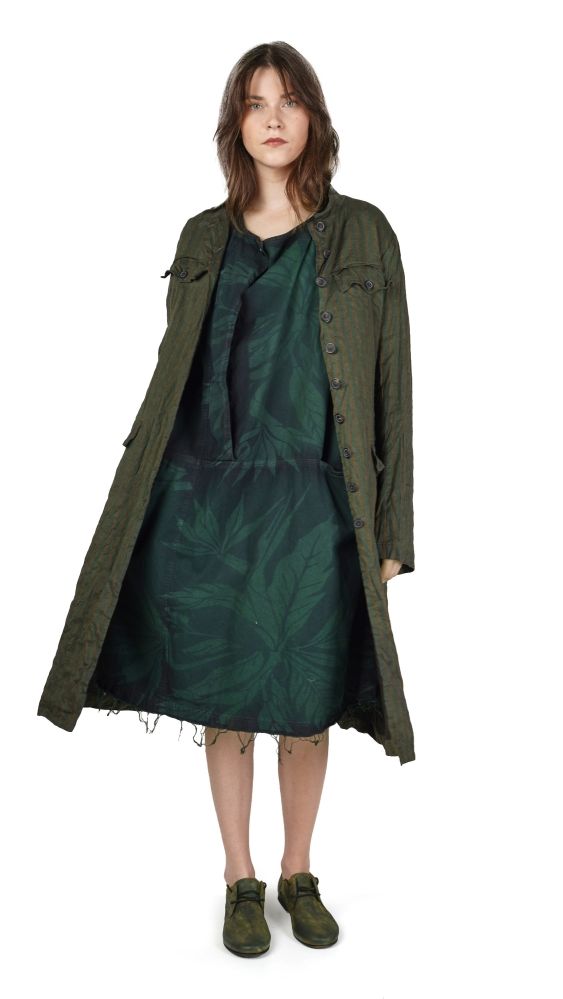 Frau trägt olivgrünen oversize-Mantel mit kurzem, gemustertem Kleid und grünen Stiefeln.