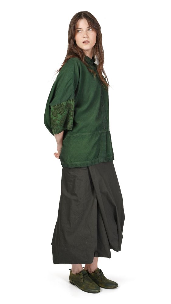 Frau trägt oversized grünes Hemd mit Stickerei, weite schwarze Hose und grüne Schuhe.