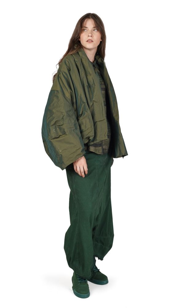 Person trägt oversized olivgrüne Jacke und weite Hose, steht seitlich posierend.