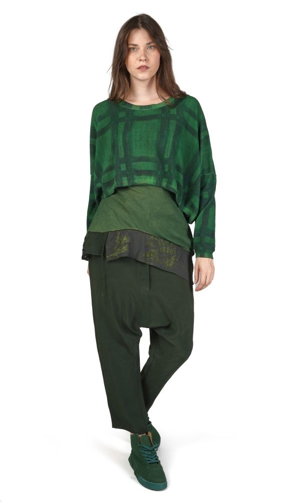 Frau trägt oversized grünes Patchwork-Top mit schwarzem Hut, grünen Haremhosen und Sneakern.