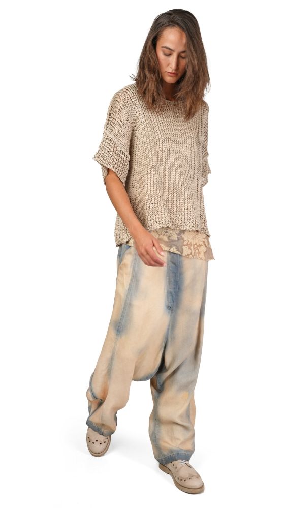 Person trägt oversized beige Strickshirt, ausgebleichte Hosen und bequeme Schuhe, nachdenklich stehend.