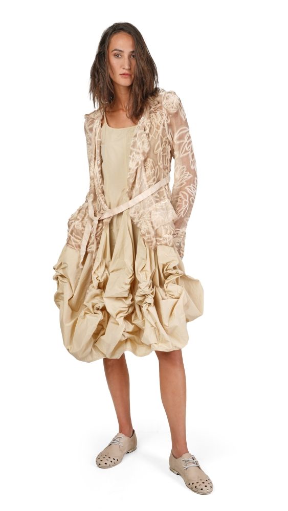 Frau trägt bohemisches, cremefarbenes Kleid mit Rüschen und transparentem Jacke, kombiniert mit flachen Sandalen.