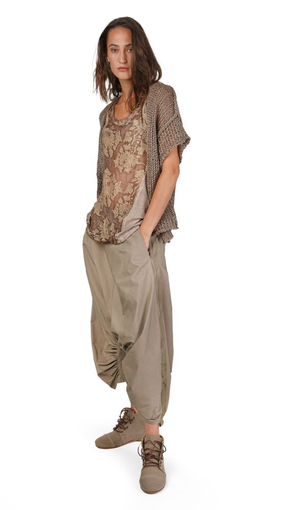 Frau trägt bequeme, oversized Bluse mit Stickerei und weite, beige Harem-Pantalons mit Sneakern.