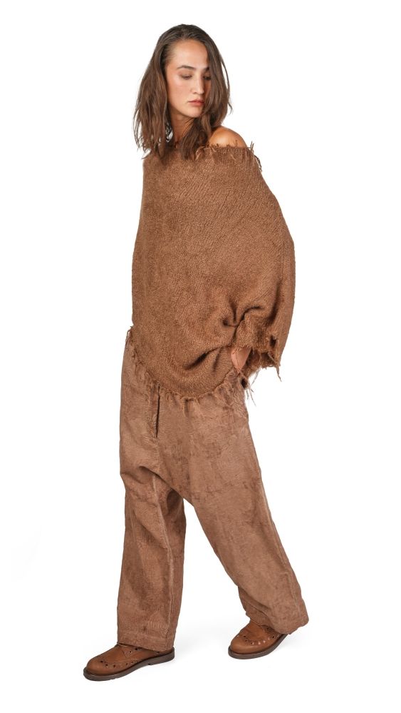 Person trägt zerfetzte, braune Overall-Kombi mit abgewetztem Look und flachen Schuhen.