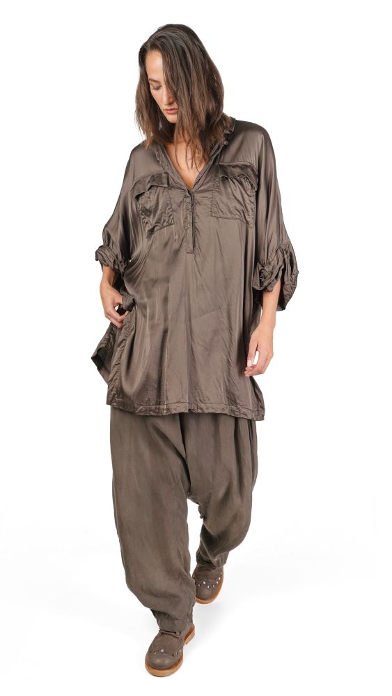 Frau trägt lockeres, langes olivfarbenes Tunika-Kleid mit weiten Hosen und flachen Schuhen.