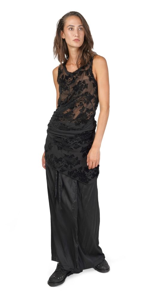 Schlanke Person im langen schwarzen Kleid mit floraler Spitzen-Optik und schwarzen Stiefeln.