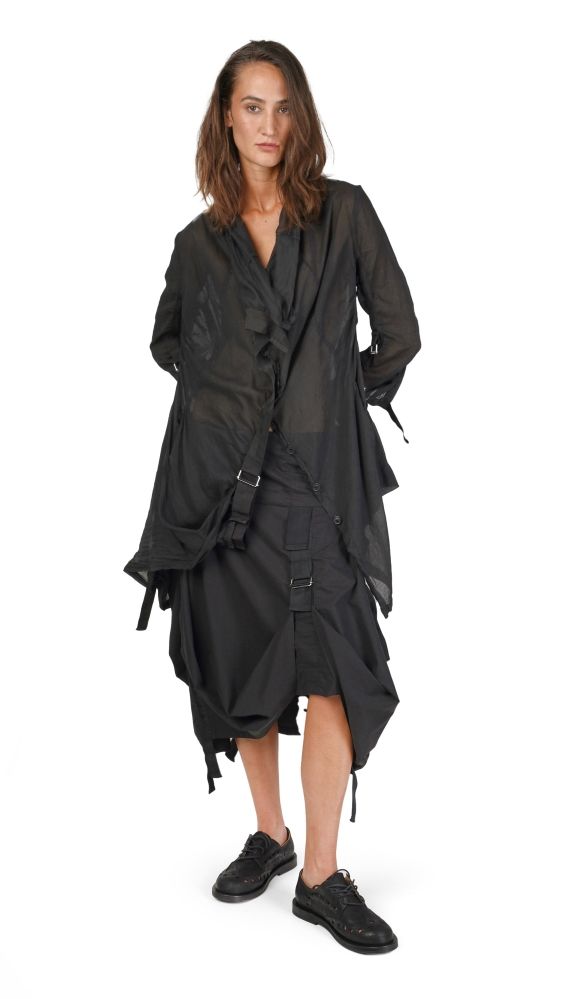 Frau trägt oversized schwarzen Mantel mit weiten Ärmeln und asymmetrischen Details, schwarze Sneaker.