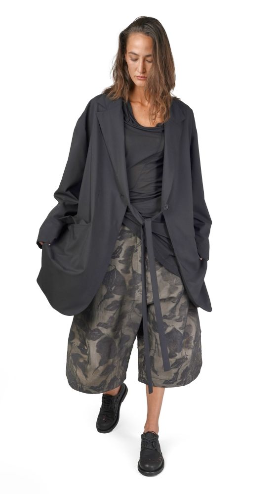 Person trägt oversized Blazer, camouflage Pantalons und schwarze Schuhe, lässig-elegant.