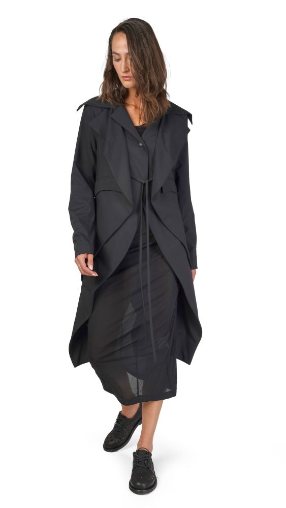 Modische Frau im langen schwarzen oversized Mantel mit asymmetrischen Details, schwarze Stiefel.