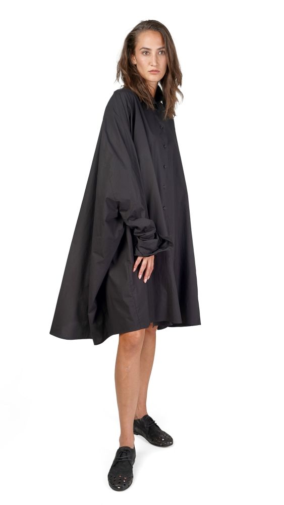 Frau trägt langes schwarzes Cape-Kleid mit kurzen Ärmeln und schwarzen Blockabsätzen.