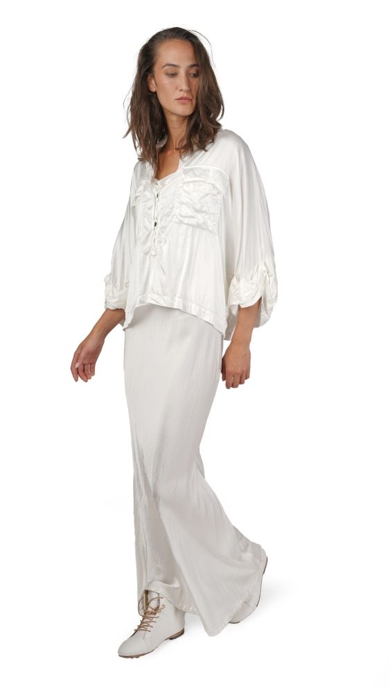 Frau trägt luftiges weißes Bluse-Pantalon-Set mit weiten Hosen und Sandalen.