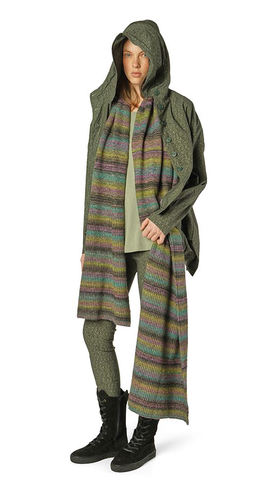Person trägt knielangen, gemusterten Strickponcho mit Hood und dunklen Leggings sowie Stiefeln.