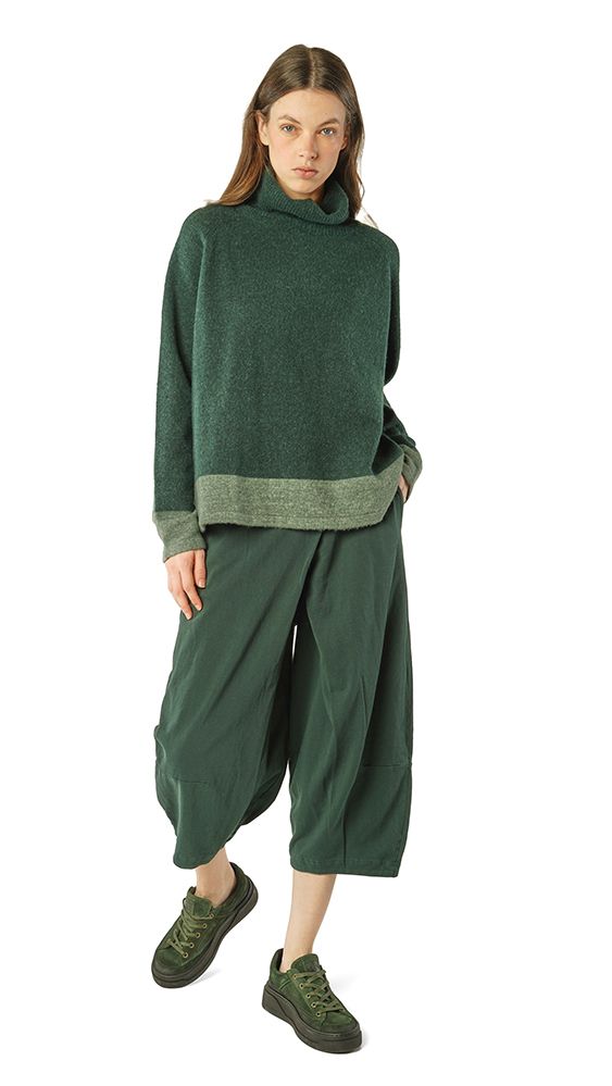Frau trägt olivgrünen oversized Pullover mit weitem Hosenrock und grüne Sneaker.