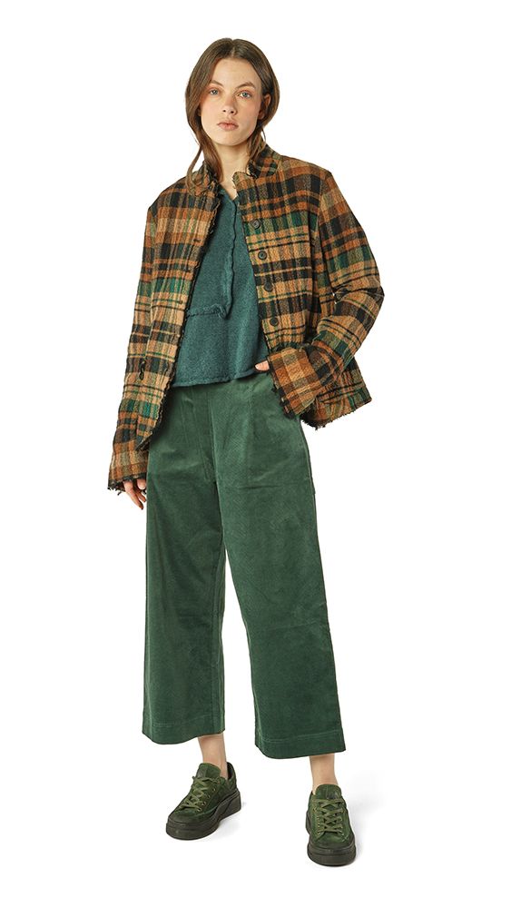 Person trägt grünen oversized-Pullover, karierte Jacke und weite Cordhose mit Sneakern.