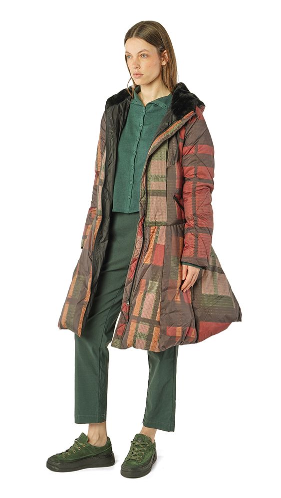 Frau trägt buntes Patchwork-Mäntelchen mit grünem Top und Hose, dunkle Sneaker.