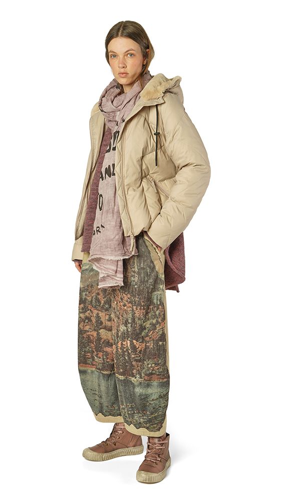 Person trägt beige Daunenjacke, bunte Patchwork-Pantalons und robuste Schuhe, mit Schal und T-Shirt darunter.