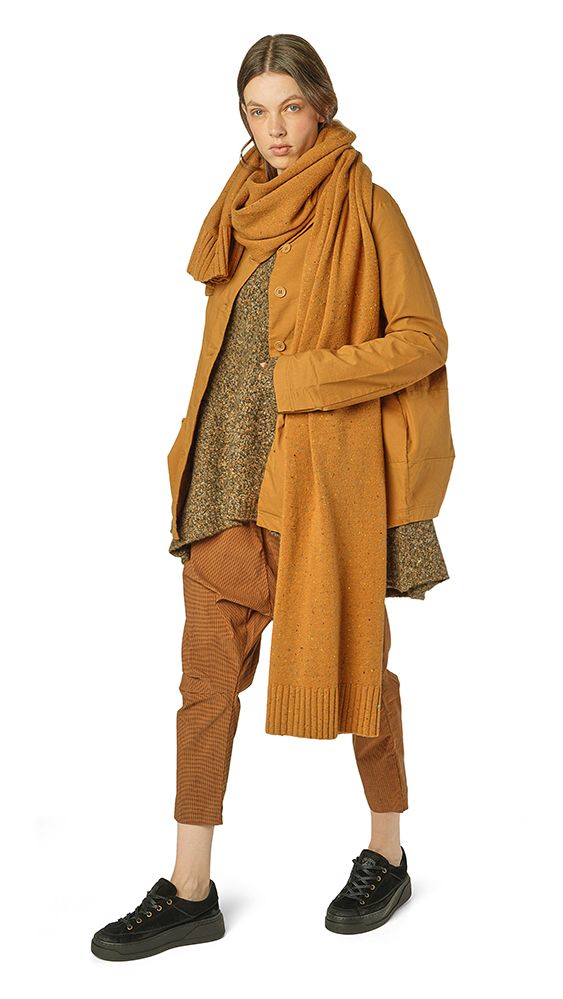 Frau trägt oversized beige Cardigan, braune Strickhose und schwarze Sneakers mit Schal.