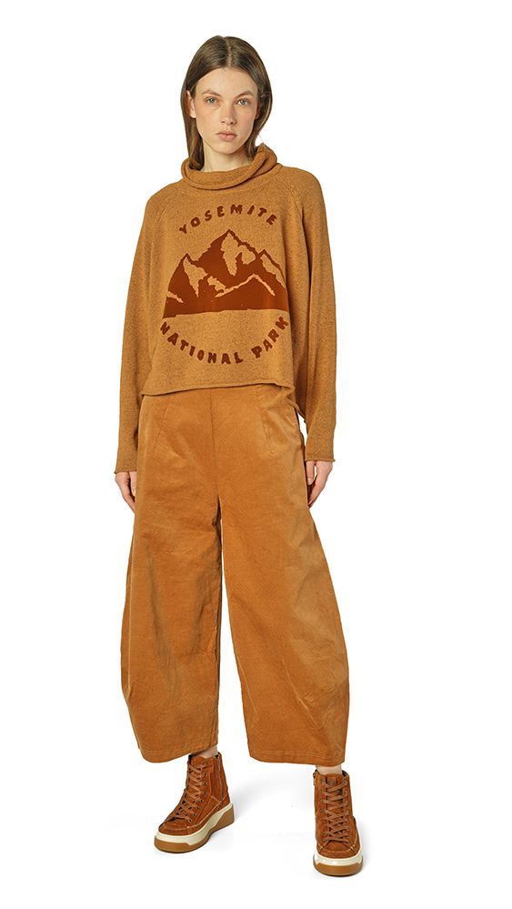 Person trägt beige Overalls mit Yosemite-Nationalpark-Aufdruck und braunen Stiefeln, cremefarbenes Top darunter.