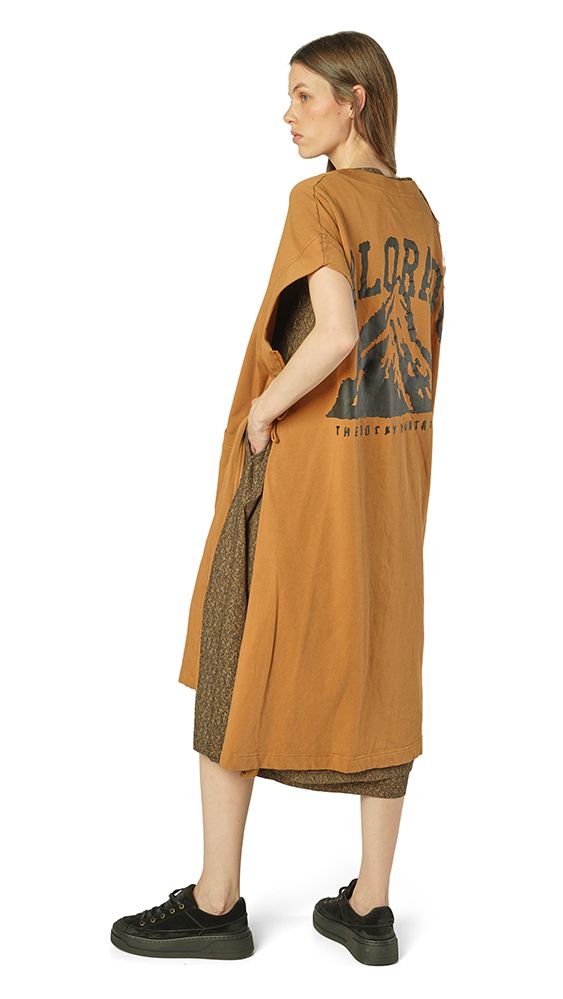 Person trägt oversized braunes Kleid mit Grafik auf dem Rücken und schwarzen Schuhen.