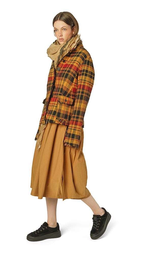 Frau trägt langen beige Rock, kariertes Cape und schwarze Sneaker, elegant und lässig.