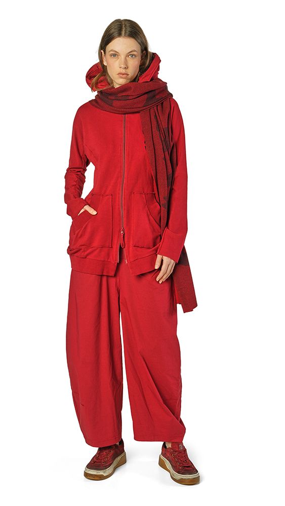 Frau trägt oversized roten Hoodie mit weitem Beinanzug und Schal, steht lässig auf hellgrauem Hintergrund.