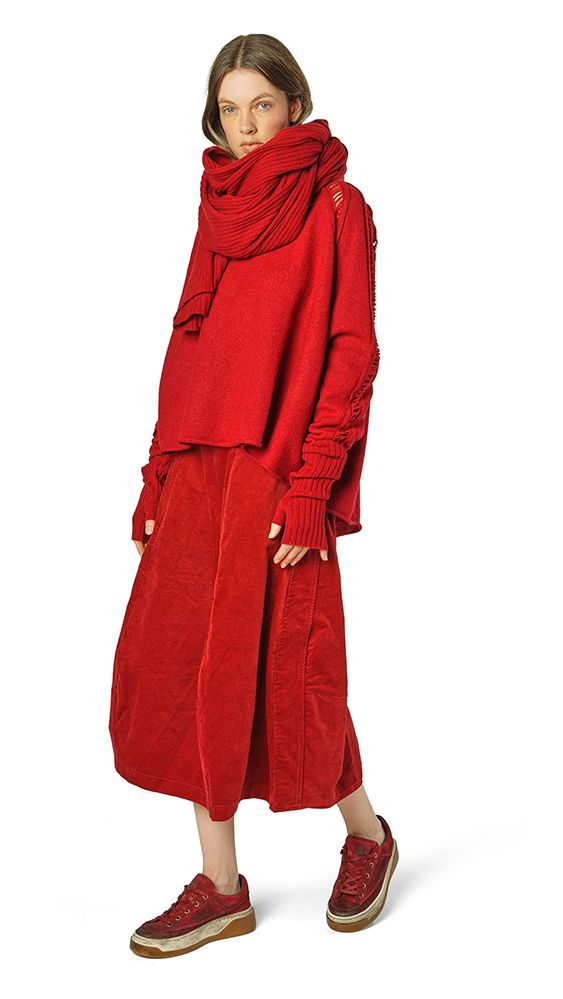 Frau trägt oversized roten Cordmantel mit Schal und Sneakern, elegant-lässig.