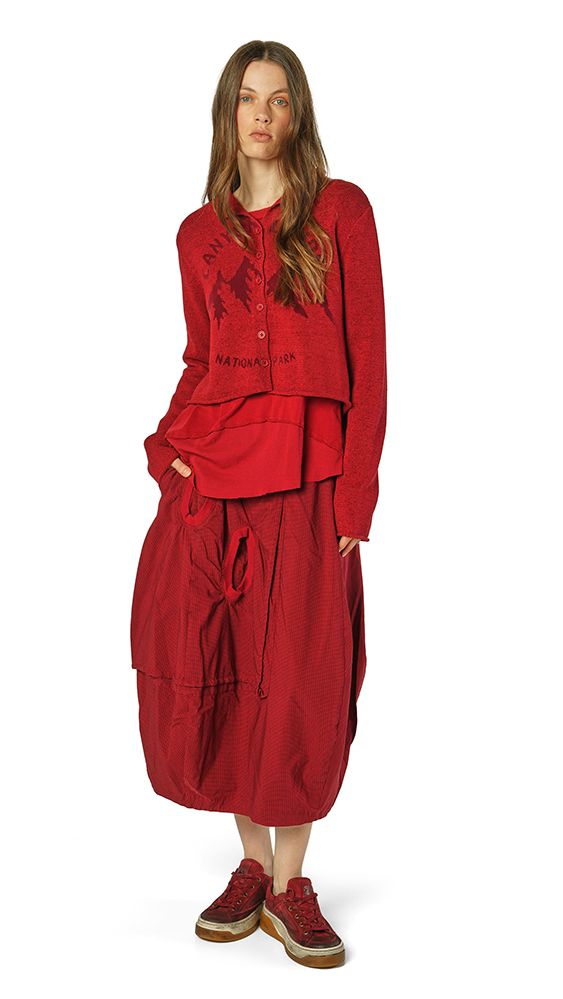 Frau trägt oversized rotes Ensemble mit weitem Rock und Sneakers, lässiger Stil.