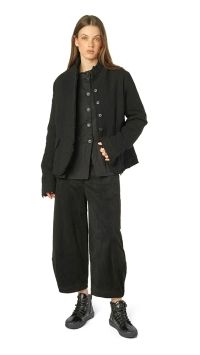 Frau trägt oversized schwarzen Blazer, dunkle Bluse und weite schwarze Hosen mit robusten Stiefeln.