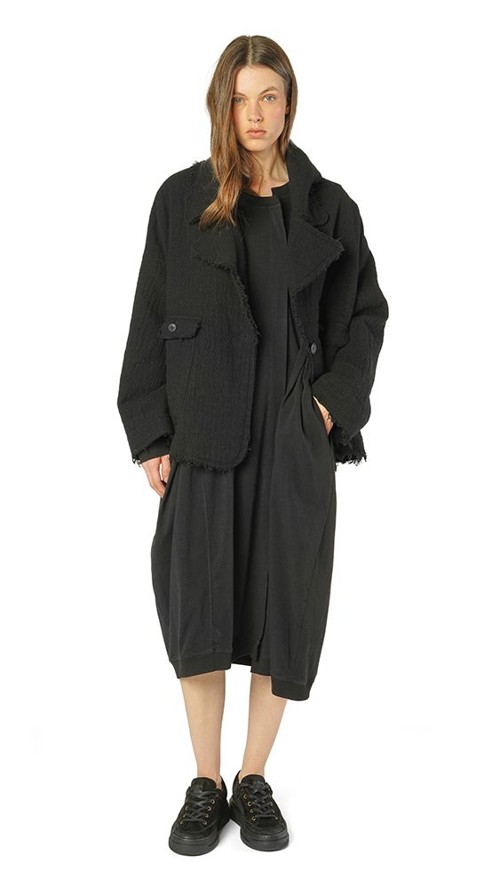 Schwarzer oversized Mantel mit Fransen, kombiniert mit schwarzem Kleid und Stiefeln.
