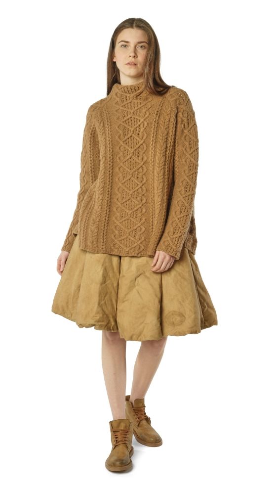Frau trägt beige, oversized Strickpullover mit kurzem, weitem Rock und braunen Stiefeln.