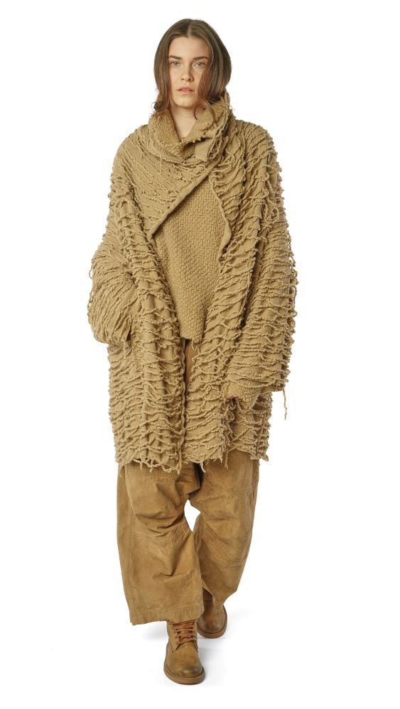 Person trägt oversized beige Strickponcho mit weitem Schnitt und beige Hosen, kombiniert mit Stiefeln.