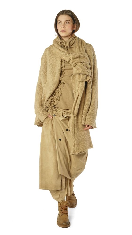 Lange, beige Wollkleidung mit asymmetrischen Fransen und knielangen Hosen, kombiniert mit braunen Stiefeln.