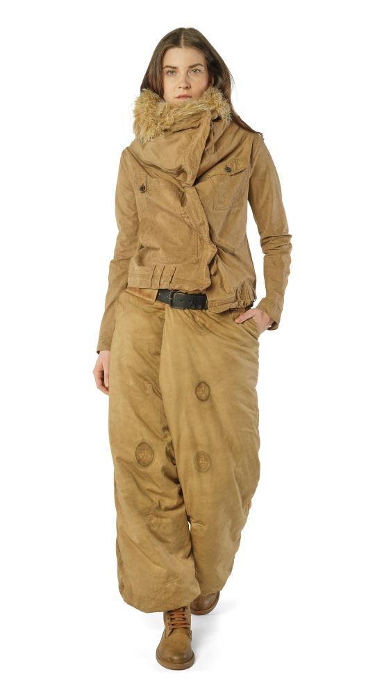 Frau in beige Überallsuit mit Fellkragen und Handschuhen, lässig posierend.