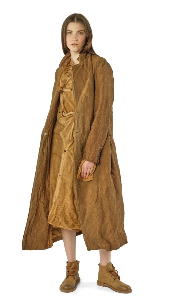 Lange, beige Wollmantel mit weitem Schnitt und abgewetzten Details, kombiniert mit kurzen Hosen und robusten Stiefeln.