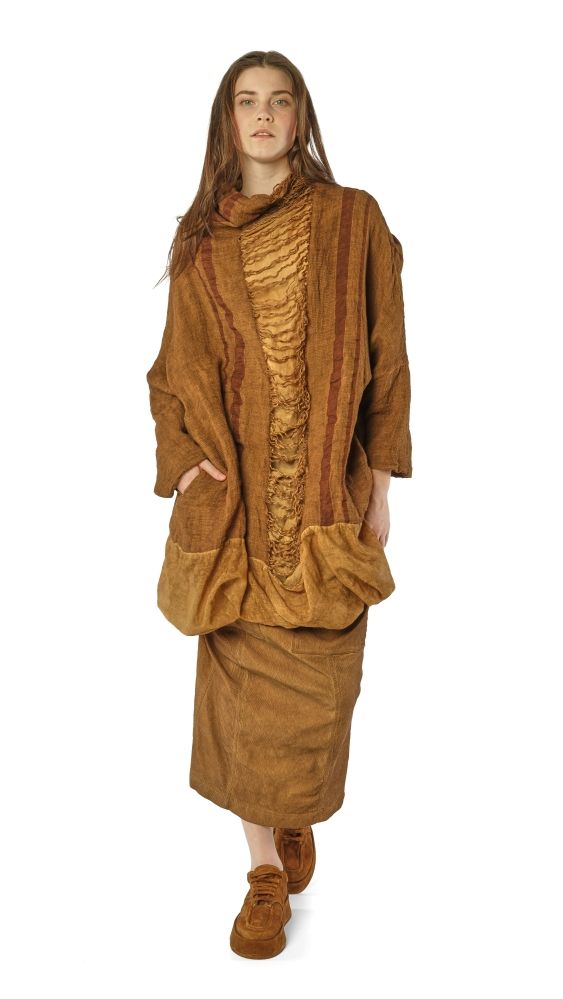 Frau trägt langes, braunes Wickelkleid mit Fransen und Anzugjacke, barfuß mit Socken.
