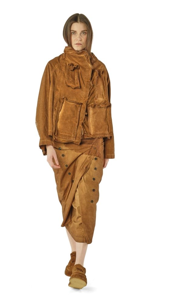 Frau trägt oversized braunes Leder-Outfit mit weitem Mantel, Hosen mit Knöpfen und Stiefeln.