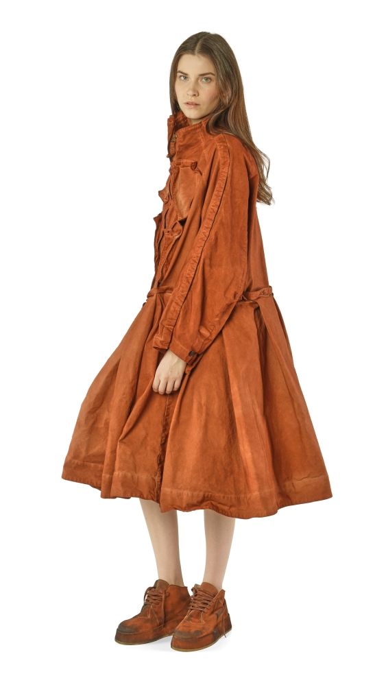 Frau in langem, rustikalem, orange-braunem Kleid mit hochgeschlossenen Ärmeln und robusten Schuhen.
