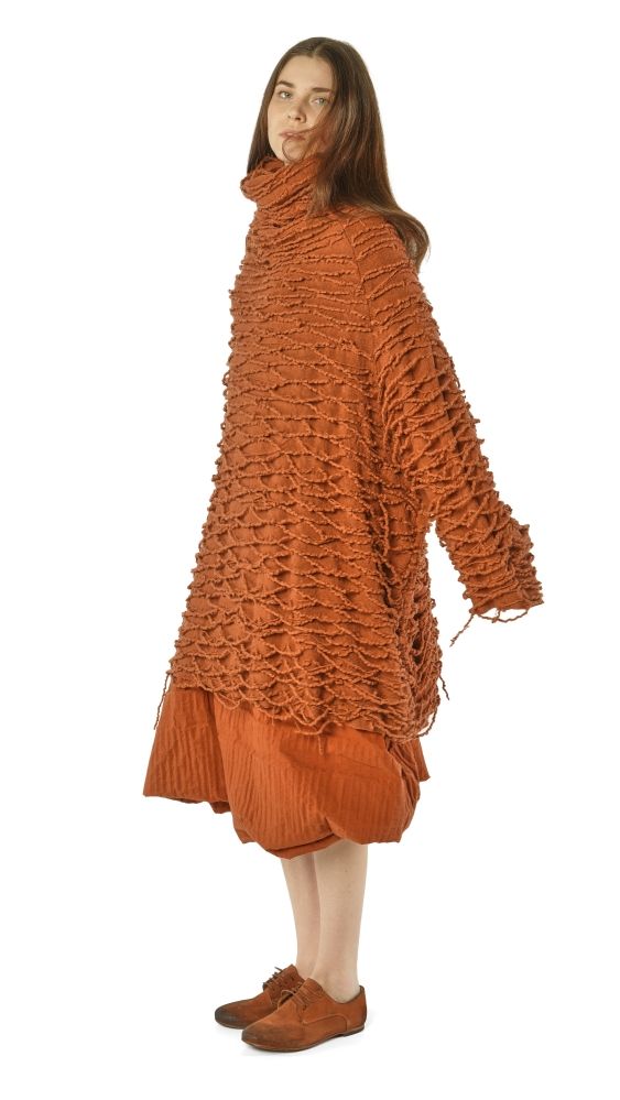 Frau trägt rustikalen, orangefarbenen Frühlingsmantel mit Fransen und Pleated-Rock, barfuß mit Schuhen.